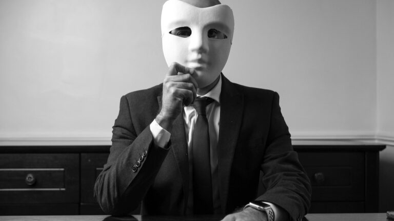 mężczyzna w garniturze trzymający maskę na twarzy podczas rozmowy exit interview – symbol ukrytych powodów odejścia pracownika